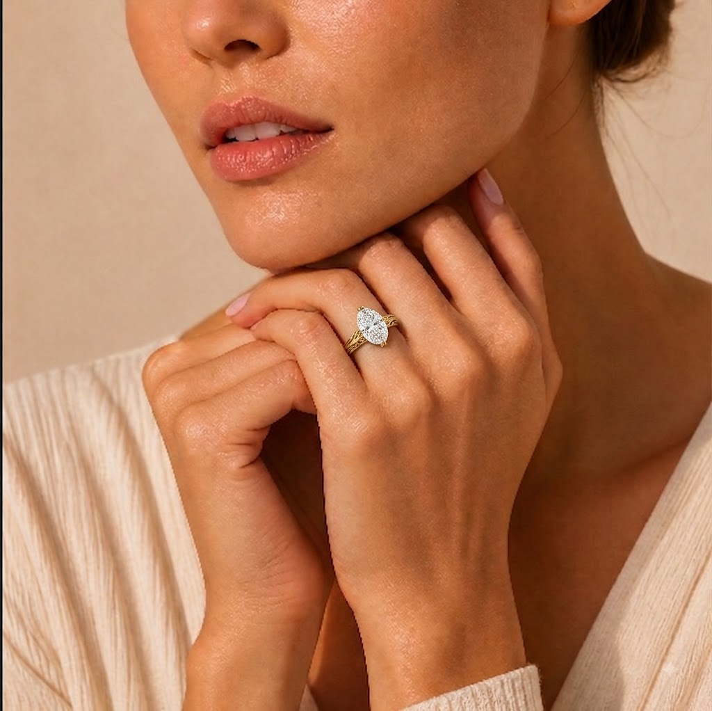 A close-up lifestyle shot of a woman wearing a gold ring with a marquise-cut clear gemstone on her finger, set against a warm beige background.
