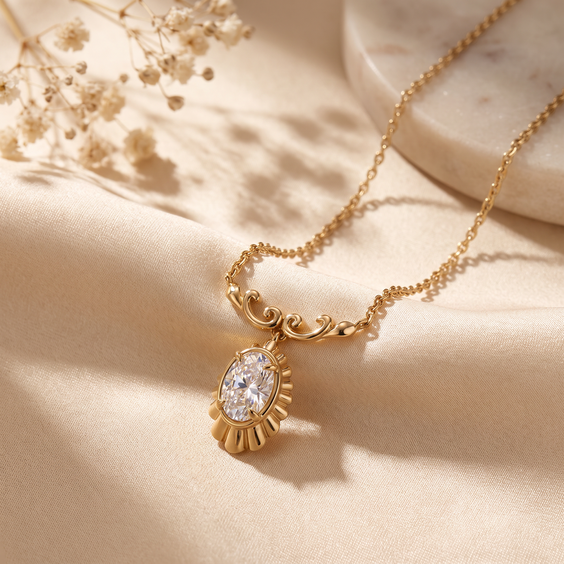A gold chain necklace with an ornate oval pendant featuring a clear faceted gemstone, styled on draped beige fabric with dried flowers and a marble slab.