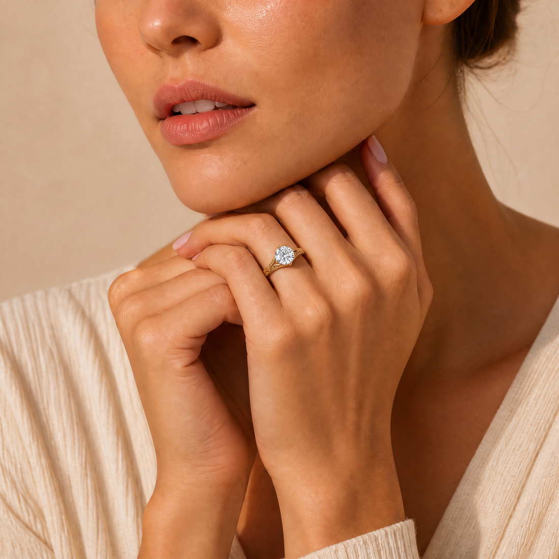 A close-up lifestyle shot of a model wearing a sparkling diamond engagement ring with a heart-shaped center stone and side stones on her ring finger. She is wearing a cream-colored ribbed knit top against a warm beige background.