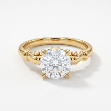 A yellow gold solitaire engagement ring with a round brilliant-cut center stone and small accent diamonds on the band, set against a clean white background.